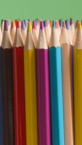 Vertical-Video-Studio-Shot-Of-Rotating-Multi-Coloured-Pencils-Against-Green-Background